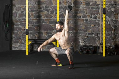 Genç sakallı ve halter pratik gömleksiz atlet spor salonunda kaçırır. Kopyalama alanı alanı konseptiyle karanlık fotoğraf. 