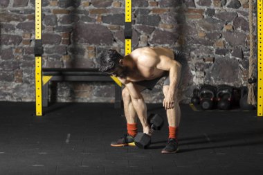 Genç sakallı ve halter pratik gömleksiz atlet spor salonunda kaçırır. Kopyalama alanı alanı konseptiyle karanlık fotoğraf. 