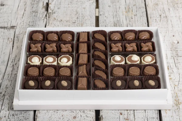 Luxury Box of Assorted handmade chocolate truffles on white wooden rustic background. Chocolates in different shapes and colors in paper box. Above angle view. Copy space for text area.