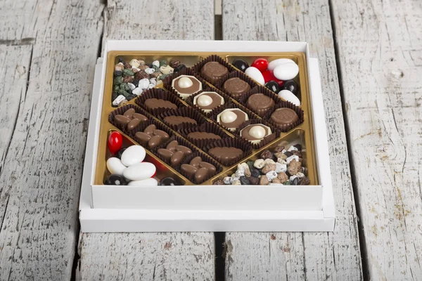 Luxury Box of Assorted handmade chocolate truffles on white wooden rustic background. Chocolates in different shapes and colors in paper box. Above angle view. Copy space for text area.