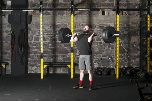 Young beard athlete training with a heavy barbell at the gym. Dark photography concept with copy space area.
