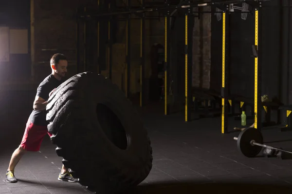 黑色衬衫男子翻转大轮胎在健身房 — 图库照片