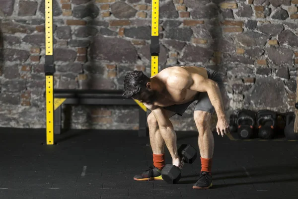 Genç sakallı ve halter pratik gömleksiz atlet spor salonunda kaçırır. Kopyalama alanı alanı konseptiyle karanlık fotoğraf. 