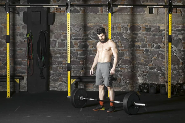 Ağır bir halter salonunda ile eğitim genç sakallı ve gömleksiz atlet. Kopyalama alanı alanı konseptiyle karanlık fotoğraf.