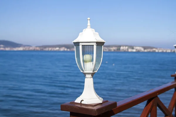close up view of decorative lamp on wooden bridge with blue sea and sky on background