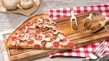 gri zemin üzerine ahşap kesme tahtası üzerinde parça İtalyan pizza ve baharat görünümü kadar kapatın