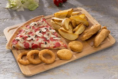 Ahşap kesme tahtası üzerinde İtalyan pizza, kızarmış soğan, patates ve tavuk nuggets görünümü kadar kapatın