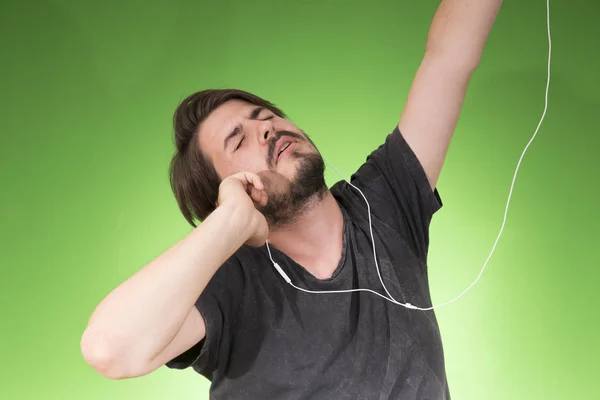 portrait of young man in earphones listening music on green backdrop