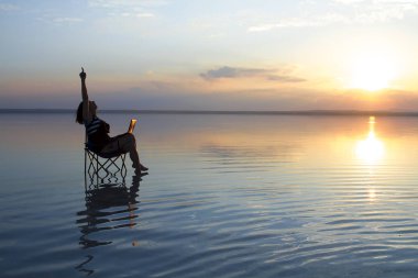 gün batımı sırasında deniz kenarındaki sandalyede istirahat laptop ile kadın