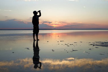 gün batımı sırasında deniz kenarındaki şişeden adam içme suyu
