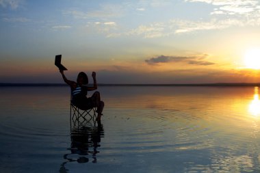 gün batımı sırasında deniz kenarındaki sandalyede istirahat laptop ile kadın