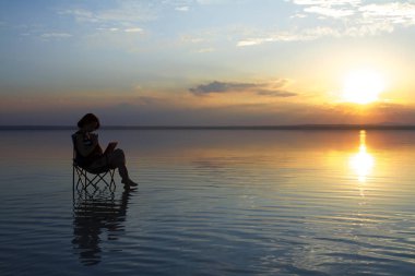 gün batımı sırasında deniz kenarındaki sandalyede istirahat laptop ile kadın