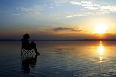 gün batımı sırasında deniz kenarındaki sandalyede istirahat laptop ile kadın