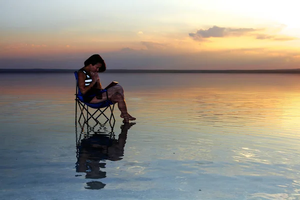 woman with laptop resting in chair at seashore during sunset