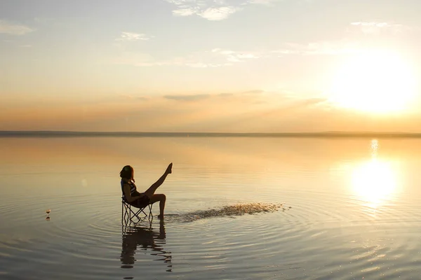 woman resting in chair at seashore during sunset