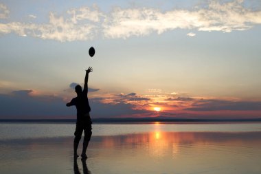 gün batımı sırasında sahil topu ile oynayan adam