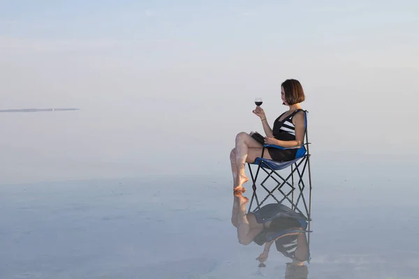 woman with glass of wine resting in chair at seashore during sunset