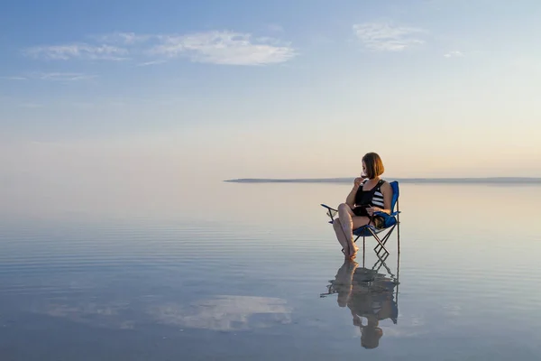 woman with glass of wine resting in chair at seashore during sunset