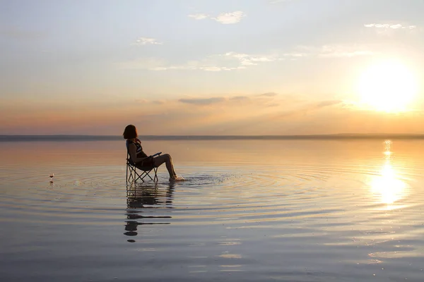 woman resting in chair at seashore during sunset