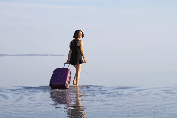 young woman with luggage walking at seashore