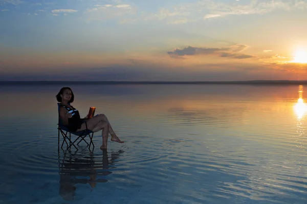 woman with laptop resting in chair at seashore during sunset