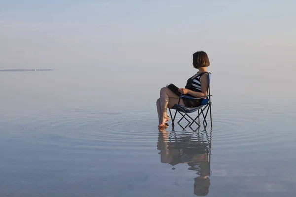 young woman with book resting in chair at seashore