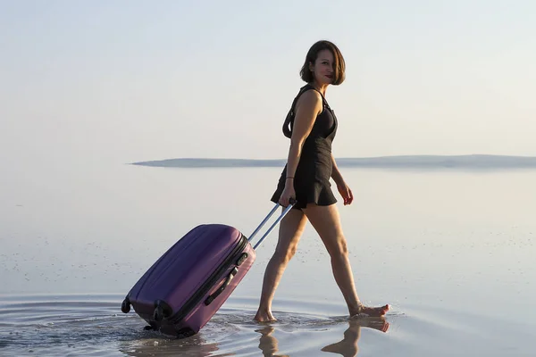 young woman with luggage walking at seashore