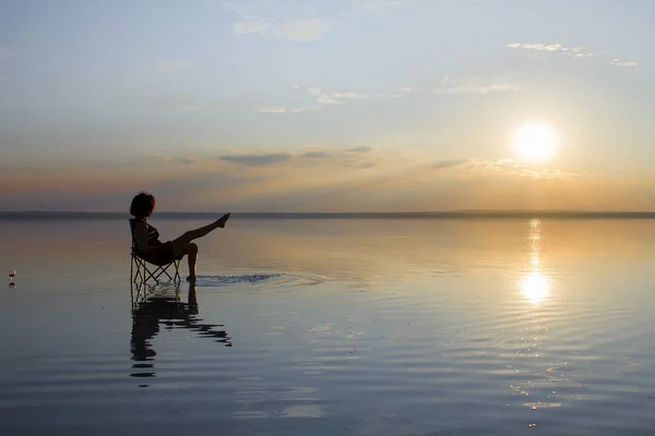 woman resting in chair at seashore during sunset