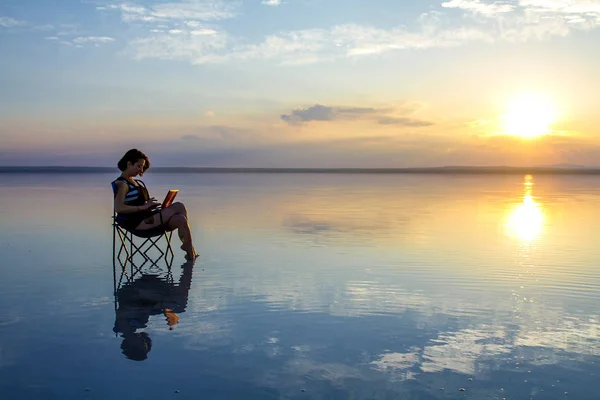 woman with laptop resting in chair at seashore during sunset