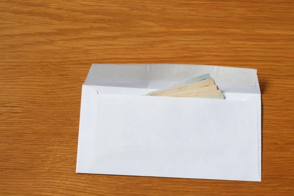 一些美元钞票的空白的白色信封在办公室的木制橡木桌子上 — 图库照片