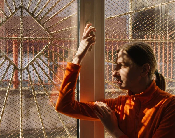 Adult young woman in orange clothes smiling and looking out the window with bars and grid, good as a concept of a psychiatric or mental hospital or a prison