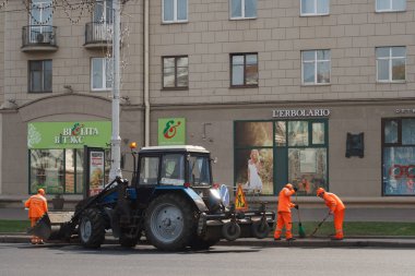 Minsk, Beyaz Rusya - 21 Nisan 2019: Yolda çalışın. Şehirde sokak temizliği: Turuncu tulumlu yol işçileri yolu süpürüp traktöre çöp koydu