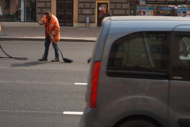Minsk, Beyaz Rusya - 21 Nisan 2019: Yolda çalışın. Şehirde sokak temizliği: Turuncu tulumlu yol işçileri yolu süpürüp traktöre çöp koydu