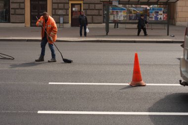 Minsk, Beyaz Rusya - 21 Nisan 2019: Yolda çalışın. Şehirde sokak temizliği: Turuncu tulumlu yol işçileri yolu süpürüp traktöre çöp koydu