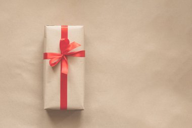 Sade geri dönüşümlü kağıda sarılıp bej arkaplanda kırmızı kurdele ile sunuluyor