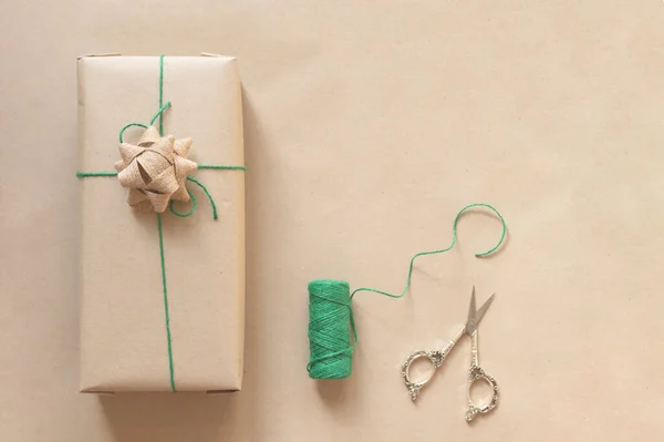 Regalo avvolto in carta riciclata semplice con filo verde e forbici su sfondo beige — Foto Stock