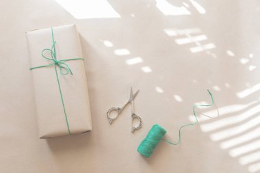 Yeşil iplik ve makas ile bej arka planda sade geri dönüştürülmüş kağıda sarılmış mevcut