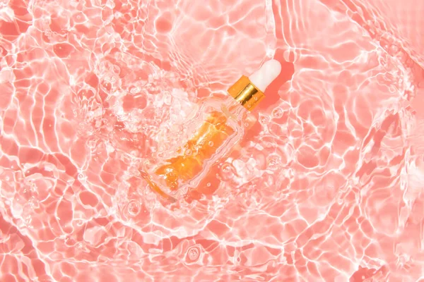 Recipiente de vidrio con aceite de belleza y pipeta en agua rosa — Foto de Stock