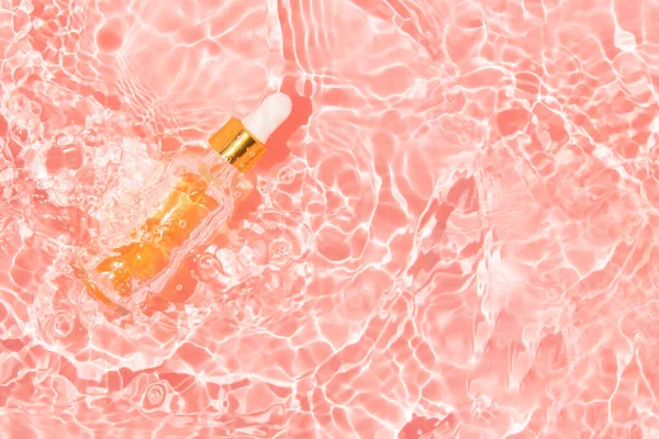 Glasbehållare med skönhetsolja och pipett i rosa vatten — Stockfoto