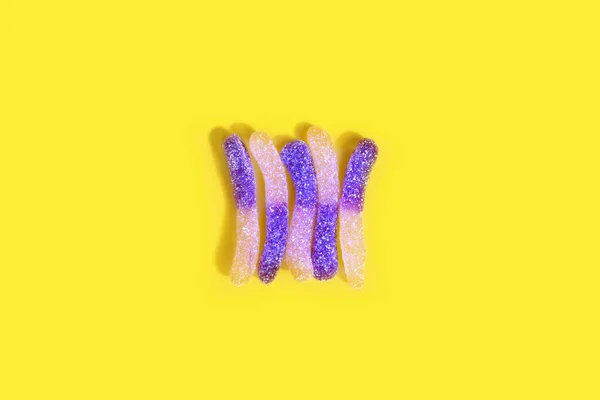 Yellow and purple sugar coated jelly worms on a yellow background — Stock Photo, Image
