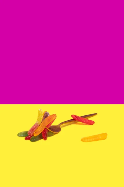 Metaliczny widelec z dżem robaki na pionowym żółtym i fioletowym tle bloku kolorów — Zdjęcie stockowe