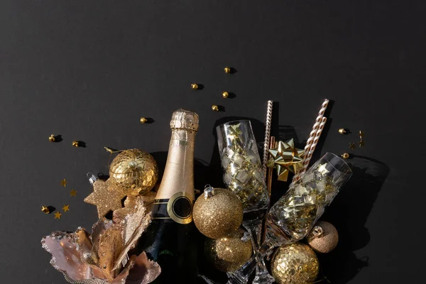 Posa piatta di una bottiglia di champagne con bicchieri di cristallo coriandoli, bagattelle e cannucce su fondo nero — Foto Stock