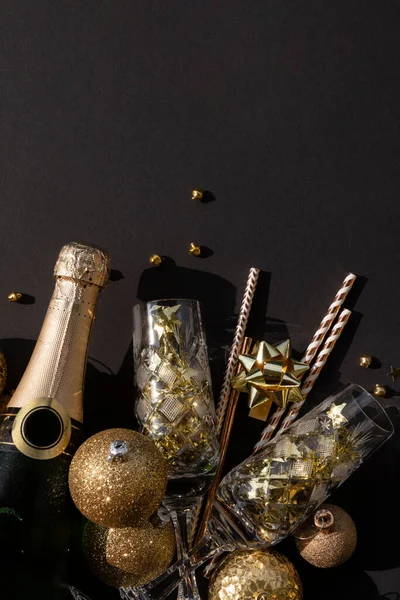 Posa piatta di una bottiglia di champagne con bicchieri di cristallo coriandoli, bagattelle e cannucce su fondo nero — Foto Stock