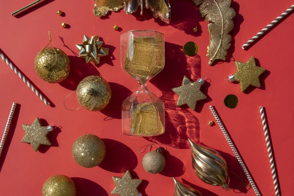 Gouden zandloper kerstballen en rietjes met confetti op een rode achtergrond — Stockfoto