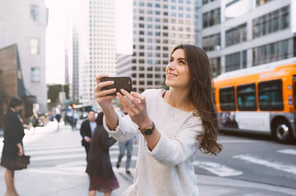 美丽的年轻女子在大街上的城市风光 市中心 手持智能手机和拍照 — 图库照片