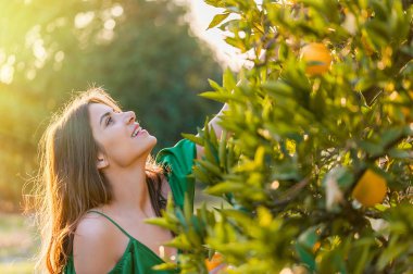 Güzel genç kadın, açık havada bir portakal bahçesi nde günbatımı gülümseyen. Sağlıklı yaşam konsepti, cilt ve saç bakım kavramı.