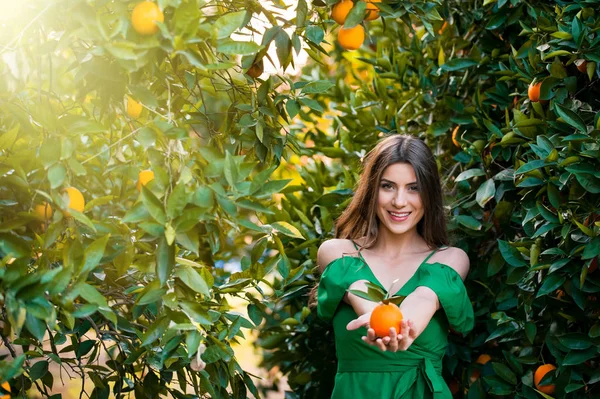 若く美しい女性 サンセット オレンジ果樹園の屋外でカメラを見て 笑みを浮かべて オレンジ色の果物を保持しています 健康的なライフ スタイルのコンセプトは 肌や髪のケアの概念 — ストック写真