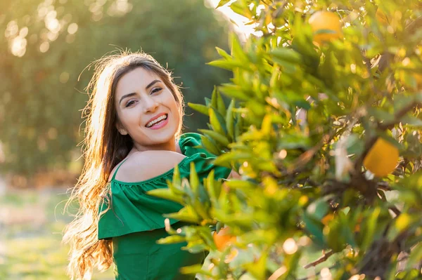 Genç ve güzel kadın, gün batımında mekanlarda turuncu bir meyve bahçesi, gülümseyen. Sağlıklı yaşam konsepti, cilt ve saç bakım kavramı.