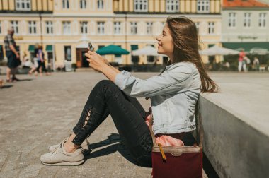 Şehir merkezinde oturan genç güzel kadın telefonunu kontrol.