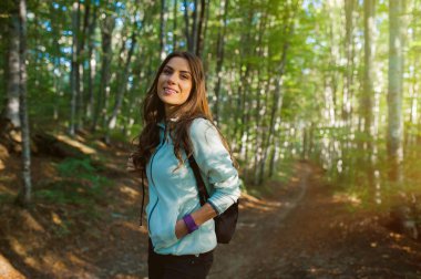 Genç kadın sonbaharda gün batımı ışığında ormanda bir sırt çantası taşıyan, ormanda bir yürüyüş.